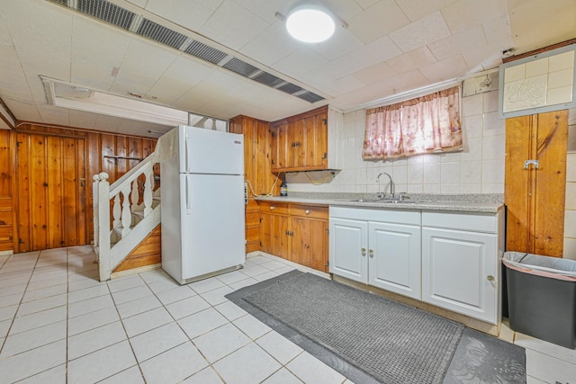 kitchen with wooden walls, light tile patterned floors, freestanding refrigerator, a sink, and light countertops