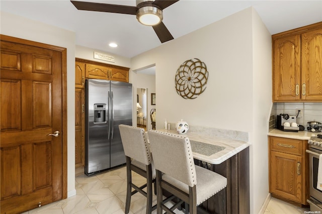 kitchen featuring brown cabinets, stainless steel appliances, tasteful backsplash, light countertops, and a kitchen bar