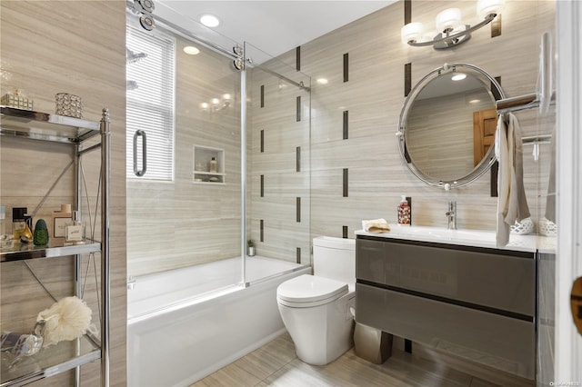 full bathroom featuring tile walls, combined bath / shower with glass door, vanity, and toilet