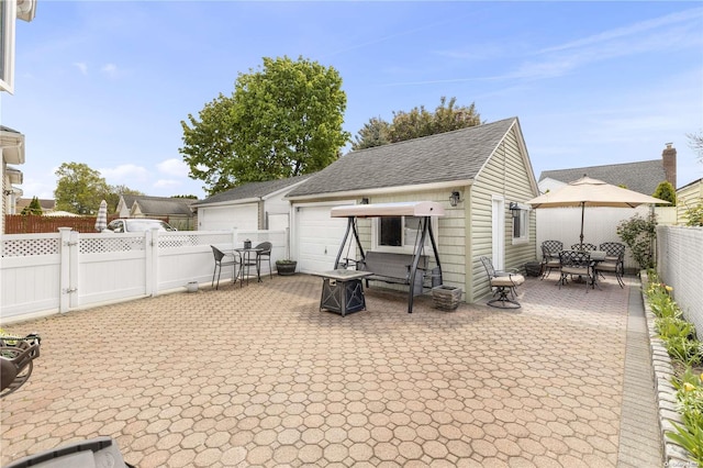 rear view of house with a fenced backyard, roof with shingles, outdoor dining area, an outdoor structure, and a patio area