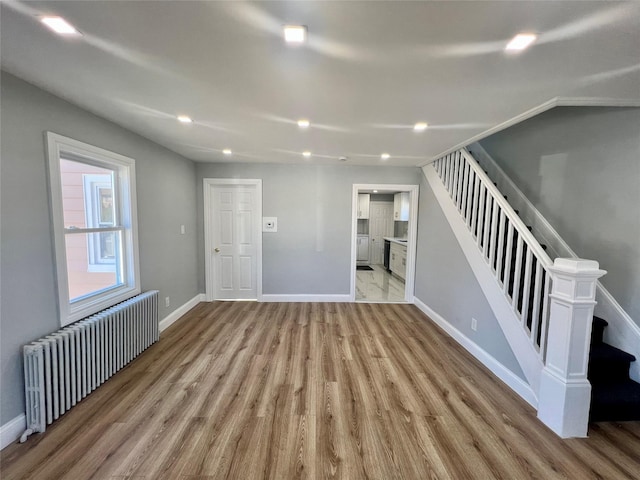 empty room with baseboards, stairway, wood finished floors, and radiator