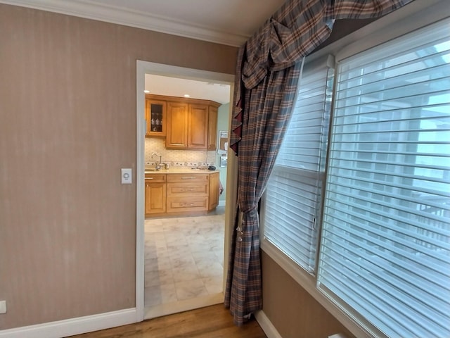 kitchen with light countertops, decorative backsplash, ornamental molding, a sink, and baseboards