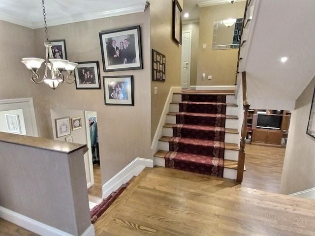 stairs featuring a notable chandelier, baseboards, crown molding, and wood finished floors