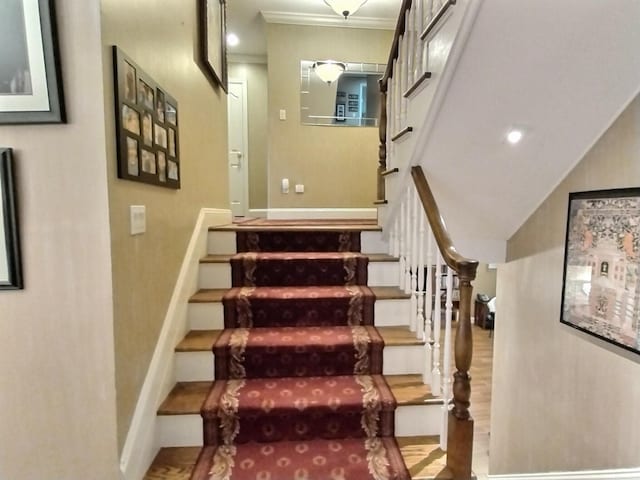 stairs with crown molding, wood finished floors, and baseboards