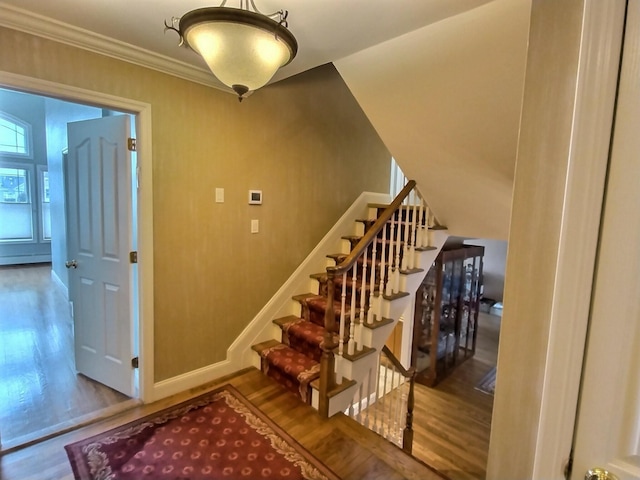 staircase with a baseboard radiator, baseboards, wood finished floors, and ornamental molding