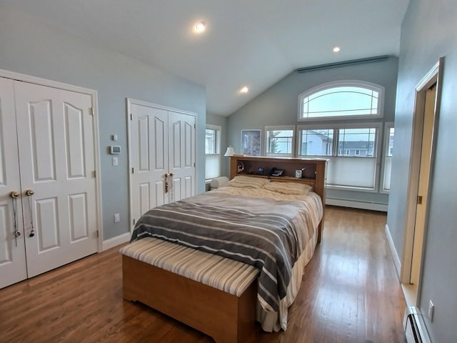 bedroom with a baseboard heating unit, wood finished floors, vaulted ceiling, and two closets