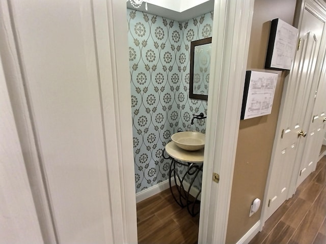 bathroom with a skylight, wood tiled floor, a sink, baseboards, and wallpapered walls