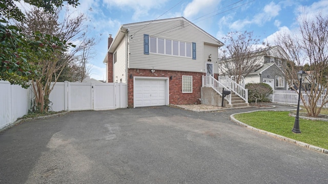 view of front of house with a gate, fence, driveway, an attached garage, and brick siding