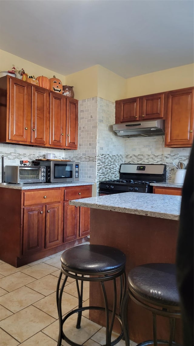 kitchen featuring under cabinet range hood, a kitchen bar, backsplash, and appliances with stainless steel finishes