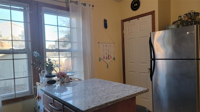 kitchen with a kitchen island, freestanding refrigerator, and light stone countertops