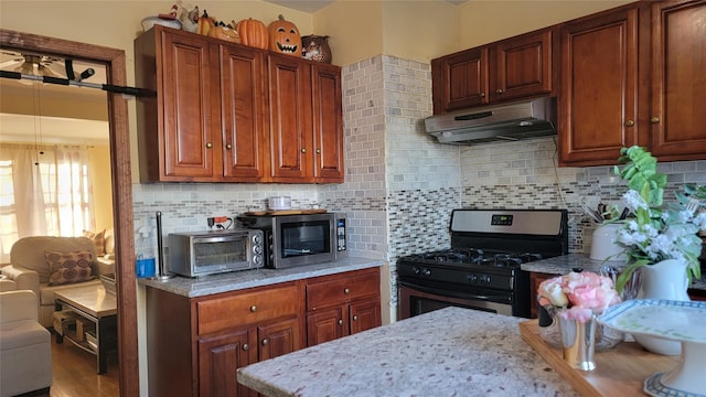 kitchen featuring light stone countertops, a toaster, appliances with stainless steel finishes, under cabinet range hood, and tasteful backsplash