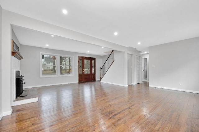 unfurnished living room featuring baseboards, stairway, wood finished floors, and recessed lighting