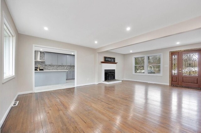 unfurnished living room with baseboards, a fireplace with raised hearth, hardwood / wood-style floors, and recessed lighting