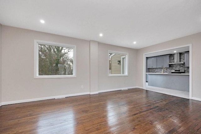 unfurnished living room featuring a sink, recessed lighting, dark wood finished floors, and baseboards