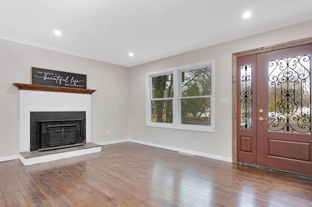 foyer entrance featuring a fireplace with raised hearth, recessed lighting, wood finished floors, and baseboards