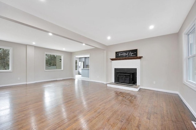 unfurnished living room featuring recessed lighting, baseboards, a fireplace with raised hearth, and hardwood / wood-style floors