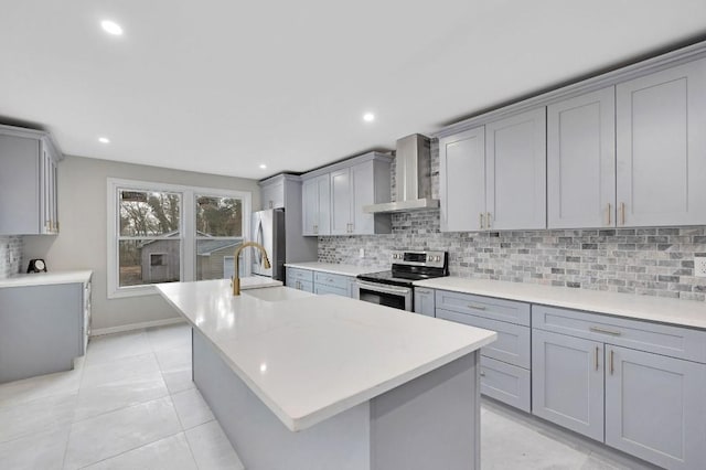 kitchen featuring appliances with stainless steel finishes, gray cabinets, wall chimney range hood, and a kitchen island with sink