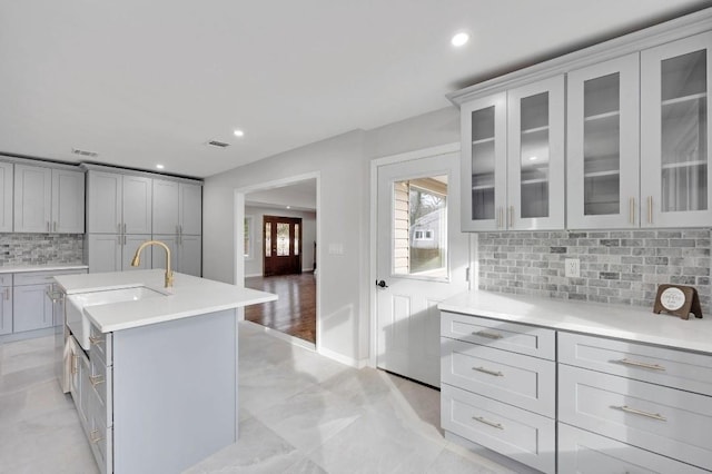 kitchen with gray cabinets, light countertops, visible vents, backsplash, and glass insert cabinets