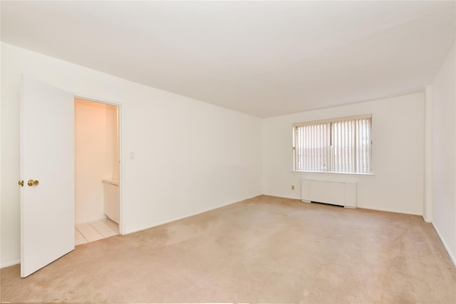 unfurnished room featuring radiator and light carpet