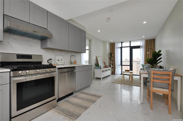 kitchen featuring gray cabinetry, under cabinet range hood, stainless steel appliances, marble finish floor, and decorative backsplash