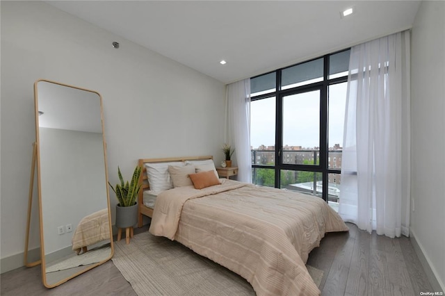 bedroom featuring baseboards, a wall of windows, wood finished floors, and recessed lighting