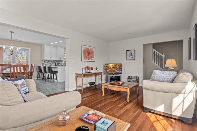 living area with stairs, an inviting chandelier, wood finished floors, and baseboards