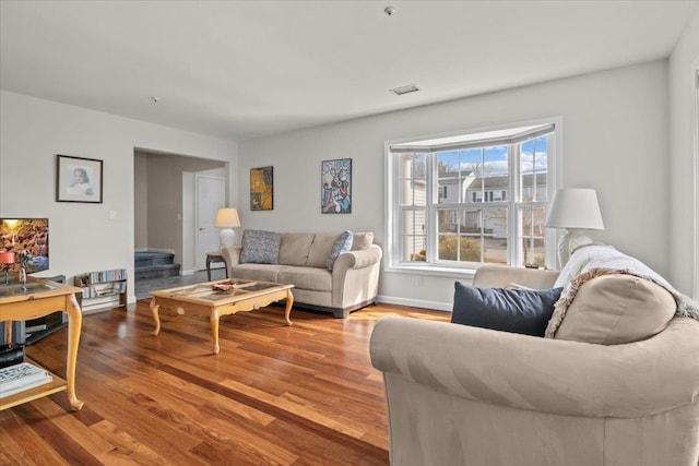 living area with visible vents, baseboards, wood finished floors, and stairs