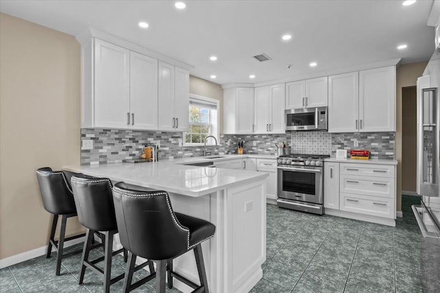 kitchen with visible vents, a sink, appliances with stainless steel finishes, a peninsula, and white cabinets