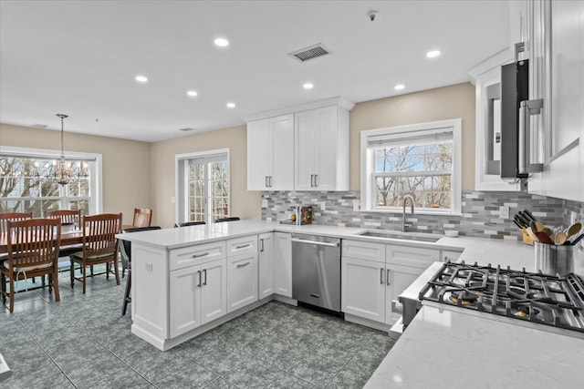 kitchen featuring visible vents, a sink, white cabinetry, a peninsula, and dishwasher