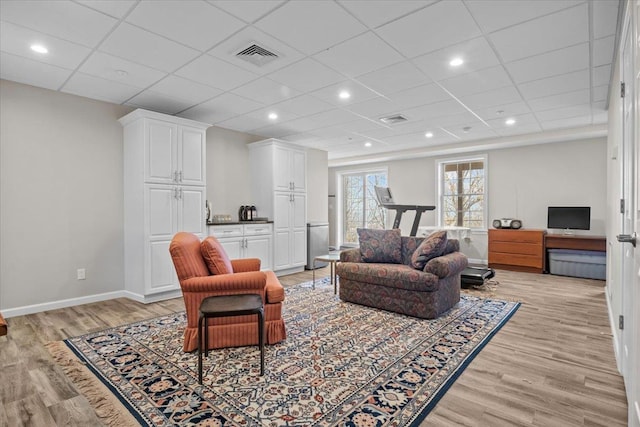 living area with light wood-type flooring, visible vents, baseboards, and a drop ceiling