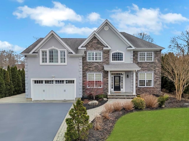 view of front facade featuring a garage, stone siding, driveway, and stucco siding