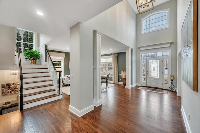 foyer entrance with dark wood finished floors, stairway, a wealth of natural light, and ornate columns