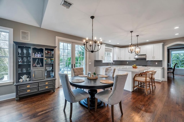 dining space featuring visible vents, arched walkways, a notable chandelier, and dark wood finished floors