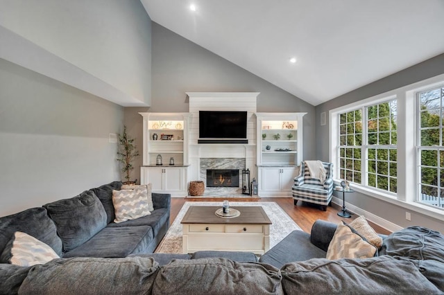 living area featuring wood finished floors, baseboards, high vaulted ceiling, recessed lighting, and a high end fireplace