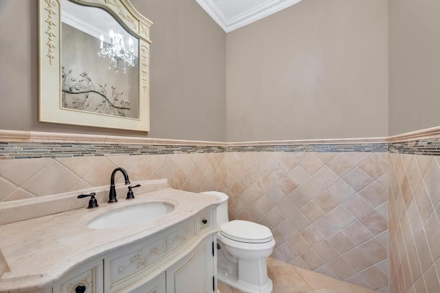 half bathroom with vanity, tile patterned flooring, wainscoting, crown molding, and toilet