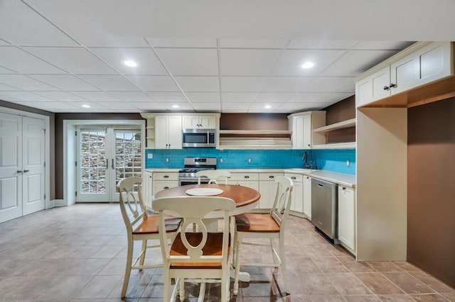 kitchen with open shelves, a sink, light countertops, appliances with stainless steel finishes, and tasteful backsplash