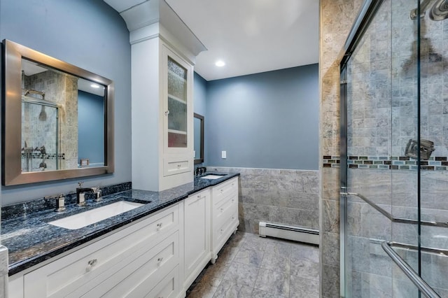 bathroom with a baseboard radiator, double vanity, a stall shower, tile walls, and a sink