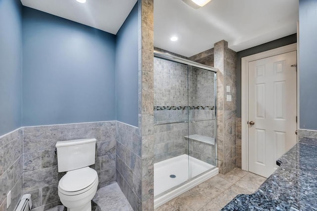 full bath with a wainscoted wall, toilet, baseboard heating, a stall shower, and tile walls