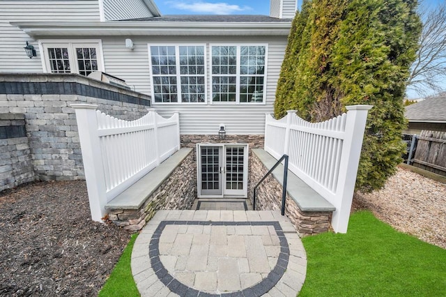 back of house featuring french doors, stone siding, and fence