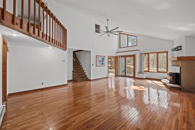 unfurnished living room featuring high vaulted ceiling, a ceiling fan, hardwood / wood-style floors, baseboards, and stairs