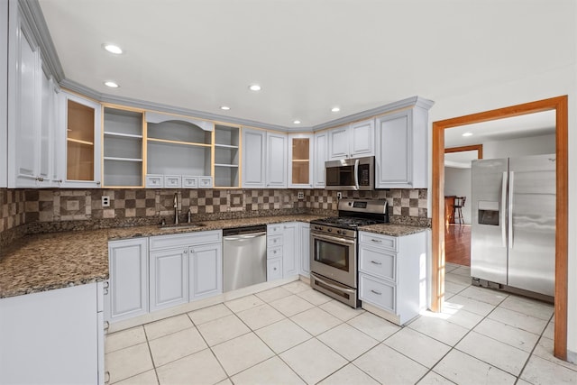 kitchen with a sink, tasteful backsplash, stainless steel appliances, dark stone counters, and light tile patterned floors