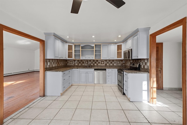 kitchen with light tile patterned flooring, a sink, appliances with stainless steel finishes, a baseboard heating unit, and tasteful backsplash