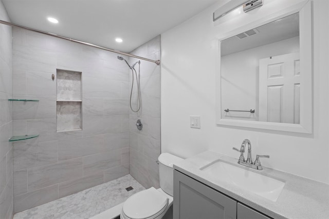 full bathroom with tiled shower, toilet, vanity, and visible vents