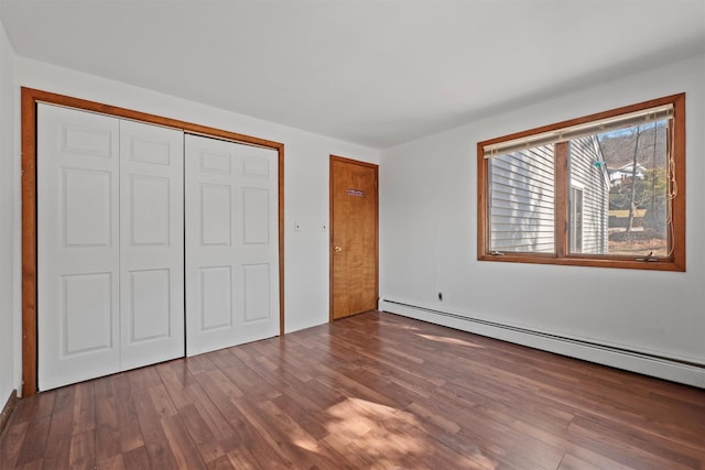 unfurnished bedroom featuring a closet, baseboard heating, and wood finished floors