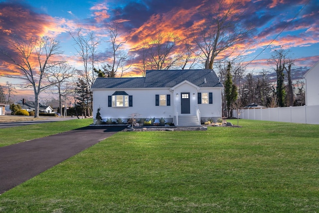 view of front of property featuring entry steps, a shingled roof, a lawn, and fence