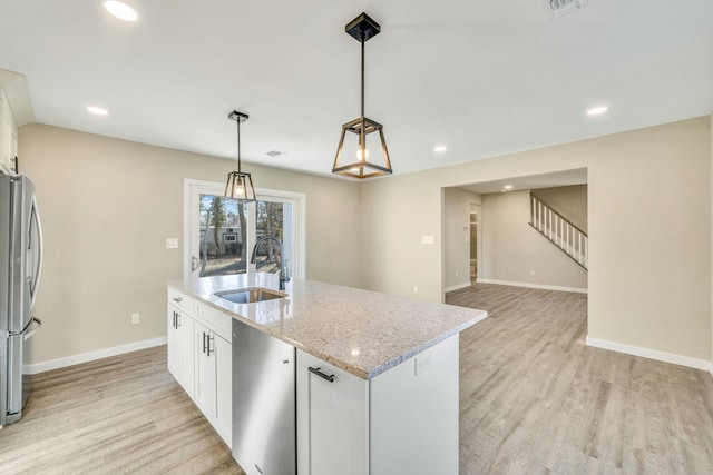 kitchen with a center island with sink, freestanding refrigerator, white cabinetry, a sink, and light wood-type flooring