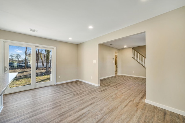 empty room with baseboards, visible vents, stairway, and light wood finished floors