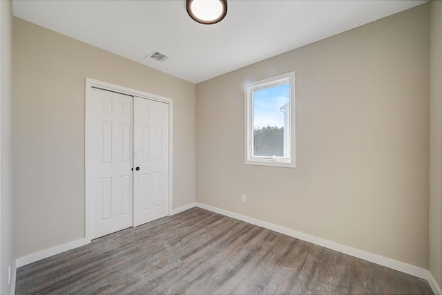 unfurnished bedroom featuring a closet, visible vents, baseboards, and wood finished floors