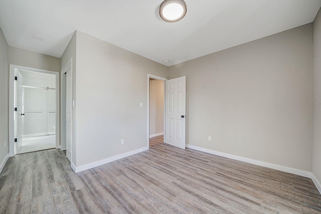 unfurnished bedroom featuring ensuite bath, wood finished floors, and baseboards