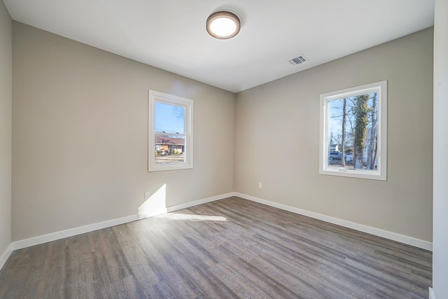 spare room with visible vents, plenty of natural light, baseboards, and wood finished floors